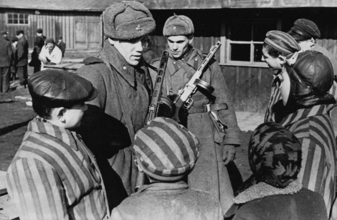Sovjetski vojaki se pogovarjajo z otroci, osvobojenimi iz Auschwitza (sovjetski vojaki ob osvoboditvi koncentracijskega taborišča Auschwitz, januar 1945, javna domena); vir: Wikimedia Commons, File: Советские солдаты общаются с детьми, освобожденными из Освенцима.jpeg, dostop 26. 1. 2026.